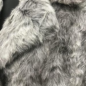 May include: Close-up of a gray faux fur fabric with a soft, fluffy texture.
