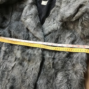May include: Gray faux fur jacket with a black lining. The jacket is measured across the chest with a yellow tape measure, showing a measurement of 22 inches.