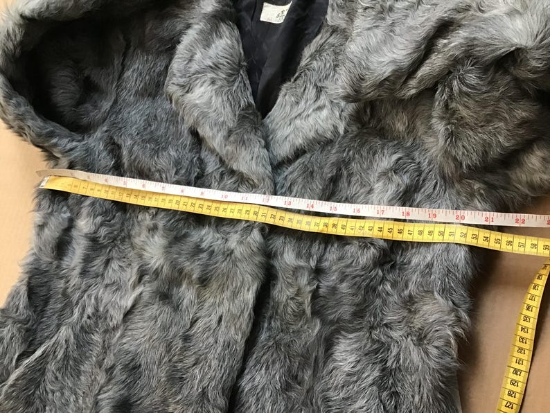 May include: Gray faux fur jacket with a black lining. The jacket is measured across the chest with a yellow tape measure, showing a measurement of 22 inches.