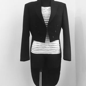 May include: A black tailcoat with a white ruffled shirt underneath. The tailcoat has a long, flowing tail and is worn on a mannequin.