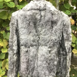 May include: A gray faux fur jacket with a collar and long sleeves. The jacket is made of soft, fluffy fur and has a classic design.