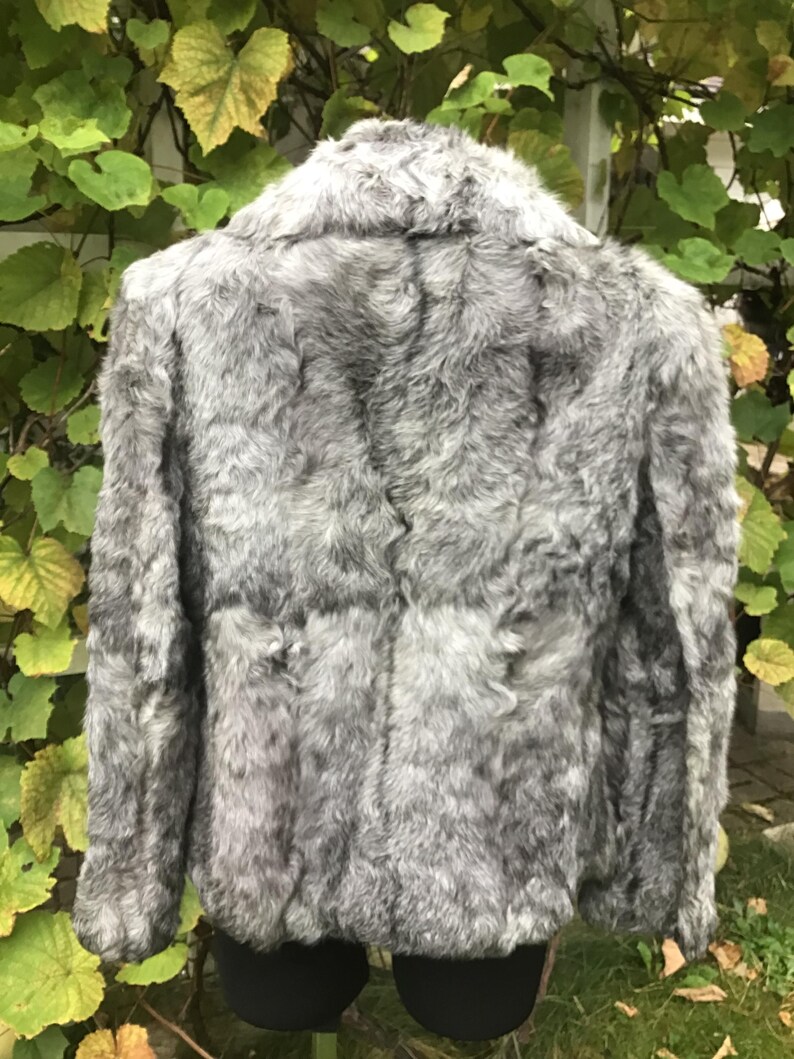 May include: A gray faux fur jacket with a collar and long sleeves. The jacket is made of soft, fluffy fur and has a classic design.