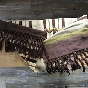 May include: Two woven brown and beige blankets with fringe. The blankets have a striped pattern and are folded on a wooden surface.