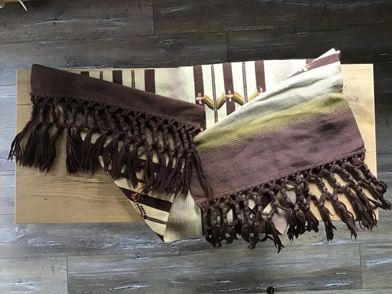 May include: Two woven brown and beige blankets with fringe. The blankets have a striped pattern and are folded on a wooden surface.