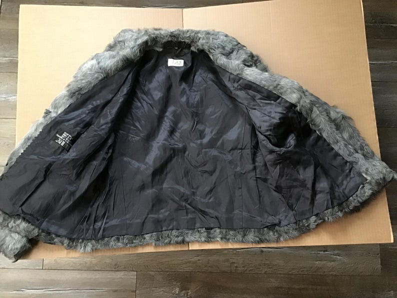 May include: A gray faux fur jacket with a black lining. The jacket is unbuttoned and the lining is visible.