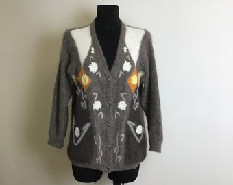 May include: A brown, white and yellow cardigan with a floral pattern. The cardigan has a v-neck and button closure.