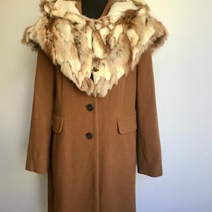 May include: A long, brown coat with a fur-trimmed hood. The coat has two buttons and two pockets. The fur trim is a mix of light and dark brown, and cream colours. The coat is displayed on a mannequin.