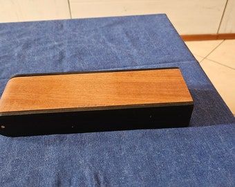 May include: A rectangular wooden box with a curved top. The top is made of light brown wood, while the sides and bottom are black. The box is resting on a blue surface.