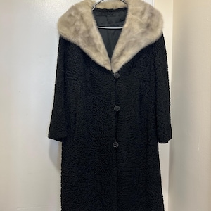 Peut inclure: Un manteau noir à manches longues avec un grand col en fourrure blanche et moelleuse. Le manteau a une fermeture à boutons et un tissu texturé.