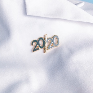 May include: A gold-colored pin with the number 2020 in black and the text "Doctor of Optometrist" in white.