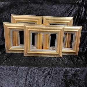 May include: Five rectangular picture frames with a gold finish and a gray inner border are arranged on a black velvet surface. The frames are empty, with no artwork or photos inside. The frames are made of wood.