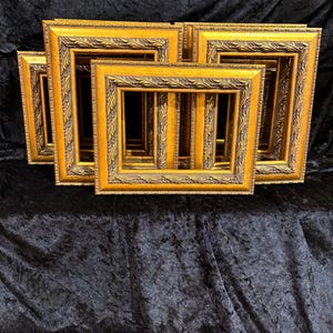 May include: A collection of rectangular picture frames featuring a metallic gold finish with dark brown recessed detailing. Each frame has a raised, repeating leaf-like pattern along the inner and outer edges, creating a textured appearance.