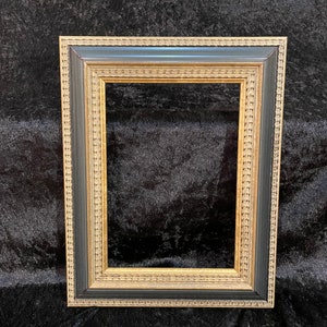 May include: A rectangular picture frame with a layered design. The frame features a gold inner border, a black middle section, and a textured outer edge. The frame is designed to hold a photograph or artwork.