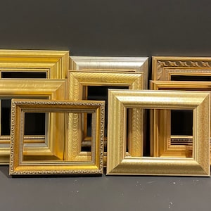 May include: A collection of ornate picture frames in various gold and silver tones. The frames have different styles, including smooth, textured, and detailed designs. The arrangement showcases a variety of sizes and shapes, suitable for artwork or photographs.