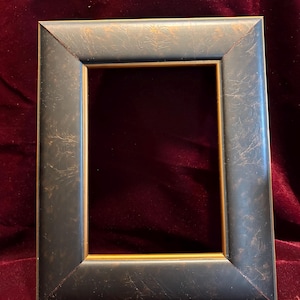 May include: A rectangular picture frame with a dark, textured finish and a gold inner edge. The frame has a distressed appearance, with hints of bronze and black. The frame is designed to hold a photograph or artwork.