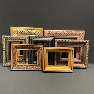 May include: A collection of eight decorative picture frames in various colors and styles. The frames include gold, brown, black, and tan, with ornate carvings and textures. The frames are rectangular and square, suitable for artwork or photos.
