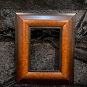 May include: A rectangular wooden picture frame with a dark brown finish and a black interior. The frame has a beveled edge and a glossy appearance, suitable for displaying photographs or artwork.