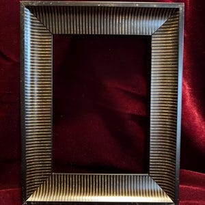 May include: A rectangular picture frame with a black finish and gold vertical stripes. The frame has a simple, yet elegant design, suitable for displaying photographs or artwork. The frame is made of a sturdy material.