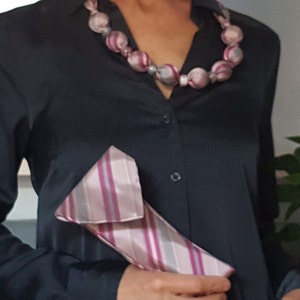 May include: A black button-down shirt with a pink and gray striped tie tucked into the pocket. The shirt has a pink and gray beaded necklace.