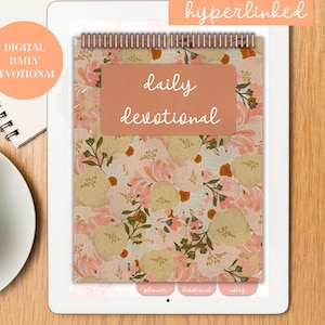 May include: A digital daily devotional displayed on a tablet. The cover features a floral pattern in pink, peach, and green. The words "daily devotional" are written on a peach-colored label. A coffee cup and notebook are visible.