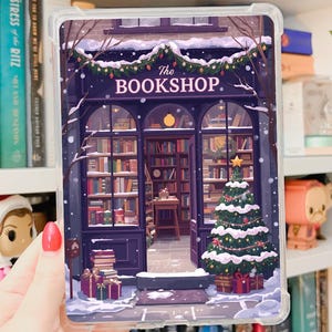 May include: Clear iPad Mini 6/7 Gen case with a winter bookstore scene, a Christmas tree, and gifts. The text "The Bookshop" is above the entrance. The word "Printable" is written in cursive at the top.