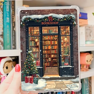 Könnte beinhalten: Transparente iPad Mini 6/7 Gen Hülle mit einer winterlichen Buchladen-Szene. Die Illustration zeigt ein Geschäft mit Weihnachtsbaum, Schnee und dem Wort "BOOKSHOP". Das Wort "Printable" steht in Kursivschrift oben links.