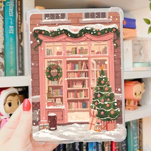 Puede incluir: Una funda transparente con una ilustración festiva de una librería en invierno. El diseño incluye un árbol de Navidad, una corona y nieve. La palabra "Printable" está escrita en la parte superior. Las palabras "FREE INSERT INCLUDED" están en la parte inferior.