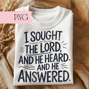 Puede incluir: Sudadera blanca de cuello redondo con el texto azul marino "I Sought The Lord, And He Heard, And He Answered". El texto tiene un aspecto texturizado y desgastado. La sudadera está doblada y expuesta sobre una superficie texturizada.