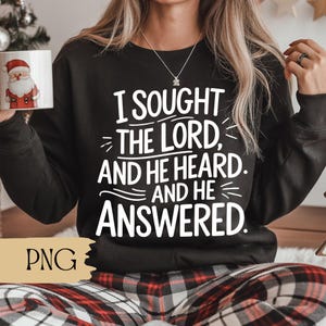 Puede incluir: Sudadera negra con el texto blanco "I Sought The Lord, And He Heard. And He Answered.". La imagen también incluye una taza blanca con un diseño de Papá Noel y pantalones a cuadros rojos y negros.