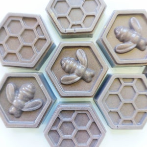 Op de afbeelding: Zeven zeshoekige zeepjes met een honingraatpatroon en een bijendesign. De zeepjes zijn donkerbruin.