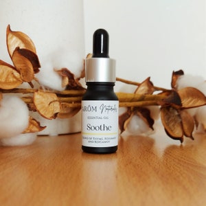 Puede incluir: Una pequeña botella negra con tapa plateada y gotero. La botella está etiquetada "Arom Naturals Essential Oil Soothe Blend of Thyme, Rosemary and Bergamot"