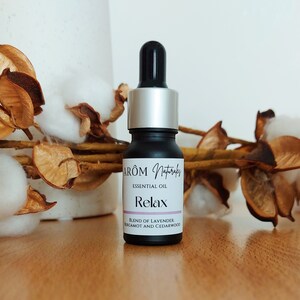 Op de afbeelding: Een zwarte glazen fles met etherische olie met het label "AROM Naturals Etherische Olie Relax Mengsel van Lavendel, Bergamot en cederhout".