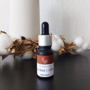 Op de afbeelding: Een klein zwart flesje met een zilveren dop en een bruin etiket met de tekst "Fragrance Oil Hazelnut Coffee Arom Suave".