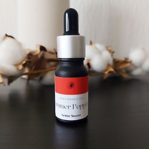 May include: A small black bottle with a silver cap and a red label. The label features a red poppy flower and the text "FRAGRANCE OIL Summer Poppies Arôm Suave".