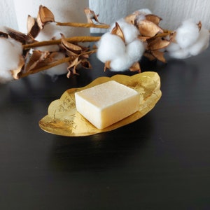 Peut inclure: Une barre de savon carrée dans un plat de couleur or avec un motif orné. Le savon est de couleur jaune pâle.