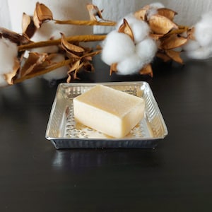 Peut inclure: Une barre de savon rectangulaire dans un porte-savon argenté. Le savon est de couleur jaune clair et a une texture légèrement rugueuse. Le porte-savon est en métal et a une finition martelée.