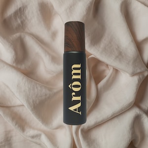 Op de afbeelding: Een zwarte fles met een houten dop en het woord "Arom" in goud gedrukt op de voorkant.