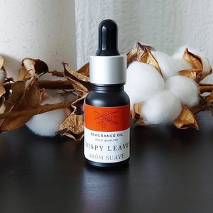 Può includere: Un piccolo flacone nero con tappo argentato e contagocce. Il flacone ha un'etichetta che dice "Fragrance Oil High Quality" e "Crispy Leaves Arom Suave".