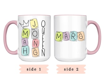 May include: White ceramic mug with a pink handle and rim. One side features the text "J MONAHG QUEEN" in colorful letter blocks with a crown. The other side displays "MARG" in similar blocks. "Side 1" and "Side 2" are written below.