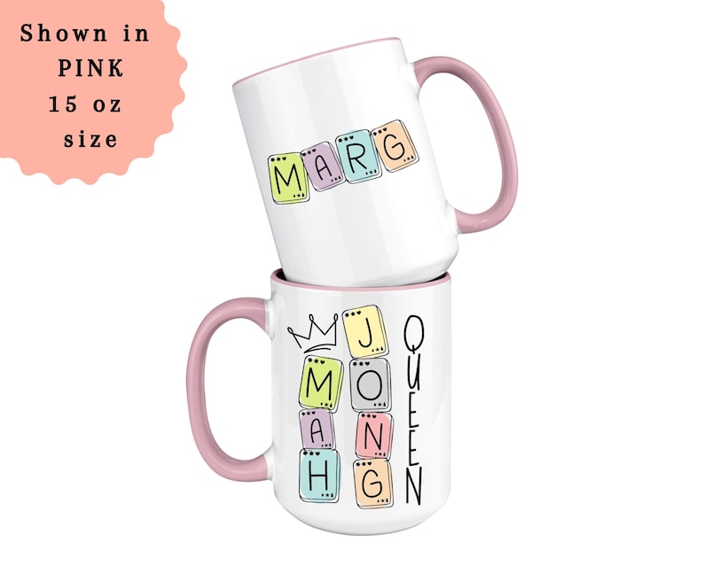 May include: Two white ceramic mugs stacked on top of each other. The top mug has the name "MARG" spelled out in colorful letter tiles. The bottom mug has the words "MOM" and "QUEEN" with a crown graphic. Both mugs have pink handles.
