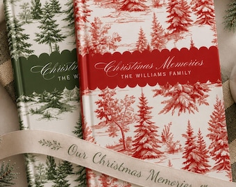May include: Two hardcover books with a toile-style forest pattern. One book features red trees on a white background with a red scalloped banner reading Christmas Memories THE WILLIAMS FAMILY. The other has green trees and a green banner.