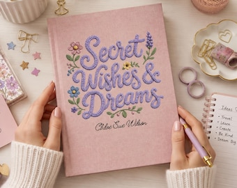 May include: A pink hardcover journal featuring the embroidered text Secret Wishes & Dreams in purple script, surrounded by small floral motifs. The name Chloe Sue Wilson is printed below in black. The cover has a textured fabric appearance.