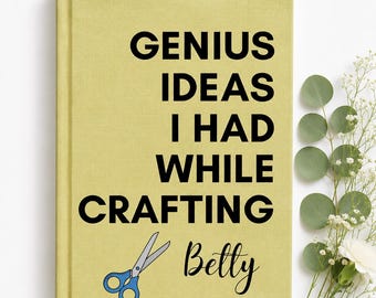 May include: A yellow hardcover notebook with the black text GENIUS IDEAS I HAD WHILE CRAFTING, the name Betty in black script, and a graphic of blue scissors with grey blades printed on the front cover.