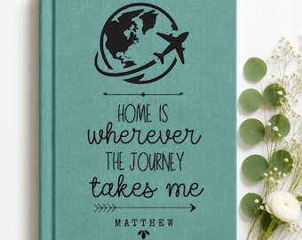 May include: A teal fabric-covered journal featuring a black graphic of a globe with an airplane silhouette. The text reads: Home is wherever the journey takes me, followed by the name Matthew and a decorative arrow design printed in black ink.