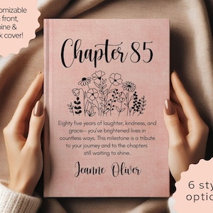 May include: A pink book cover with the text "Chapter 85" in black script, featuring a floral illustration. The cover also includes the text "Eighty five years of laughter, kindness, and grace..." and the name "Jeanne Oliver".