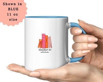 May include: White ceramic mug with a blue interior and handle. The mug features a stack of illustrated books in shades of orange and pink, with the text "chapter 30 emma". The mug is 11 oz.