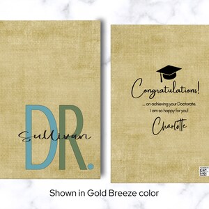 May include: A graduation card with a gold background and a black graduation cap. The card says "Congratulations! ... on achieving your Doctorate. I am so happy for you! Charlotte". The front of the card has a blue and green "DR" with the name "Sullivan" underneath.