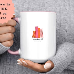 May include: White ceramic mug with a pink interior and handle. The mug features a stack of illustrated books in shades of pink and orange, with the text "chapter 40 emma". The mug is 15 oz in size.