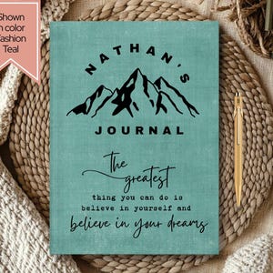 May include: Teal-colored journal with the name "Nathan's" above a mountain graphic and the word "JOURNAL" below. The journal has the quote "The greatest thing you can do is believe in yourself and believe in your dreams."