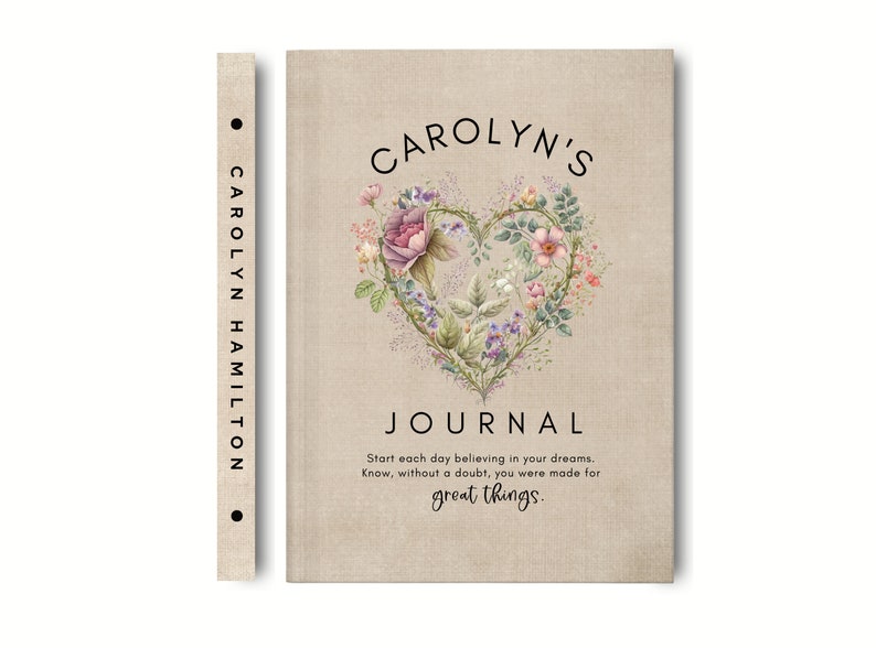 May include: A beige journal with a textured cover featuring a heart-shaped floral illustration, the text CAROLYN'S JOURNAL, and the quote Start each day believing in your dreams. Know, without a doubt, you were made for great things. The spine reads CAROLYN HAMILTON.